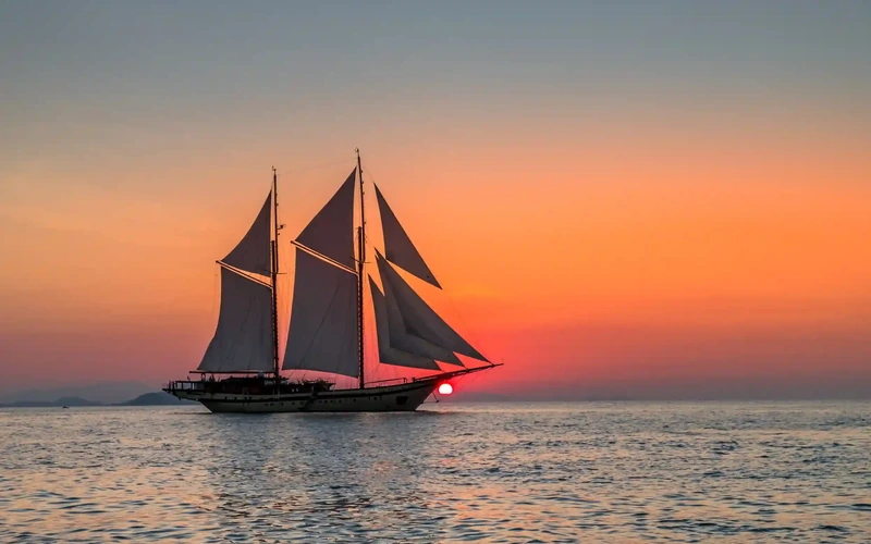A sailing vessel silhouetted against an orange sunset