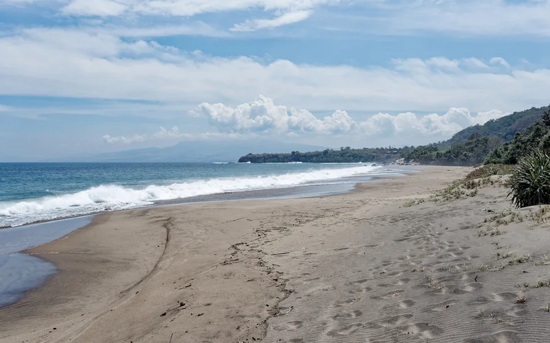 Empty sand beach running along the Flores coastline under a bright sky