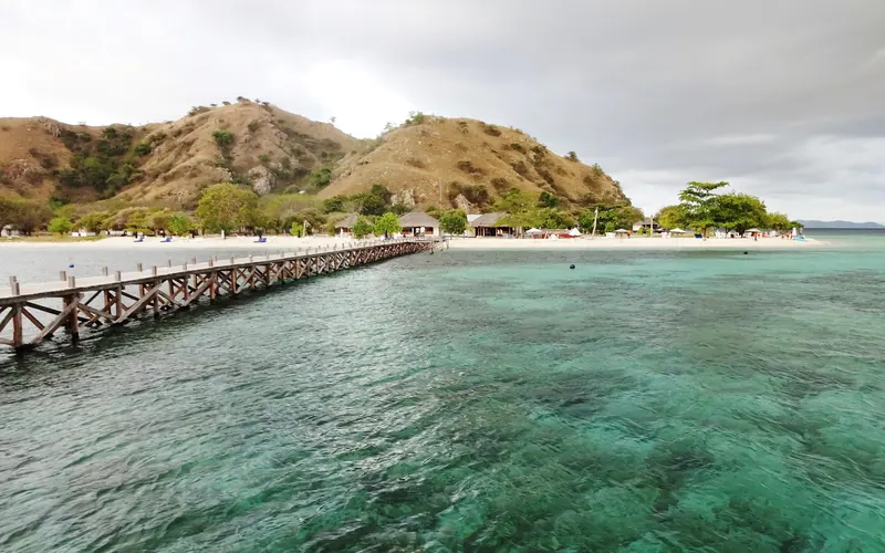 Wooden jetty reaching over clear turquoise water toward a low green island