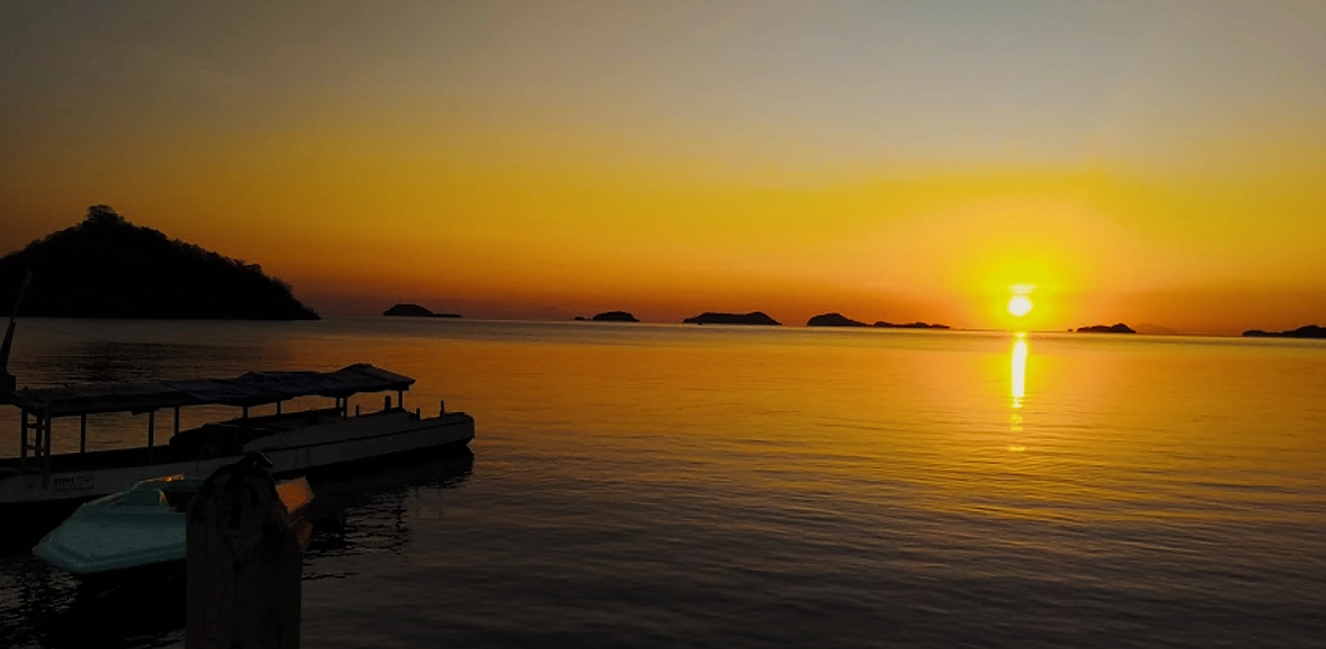 Sunset over the water at Riung, with wooden day boats moored along the pier