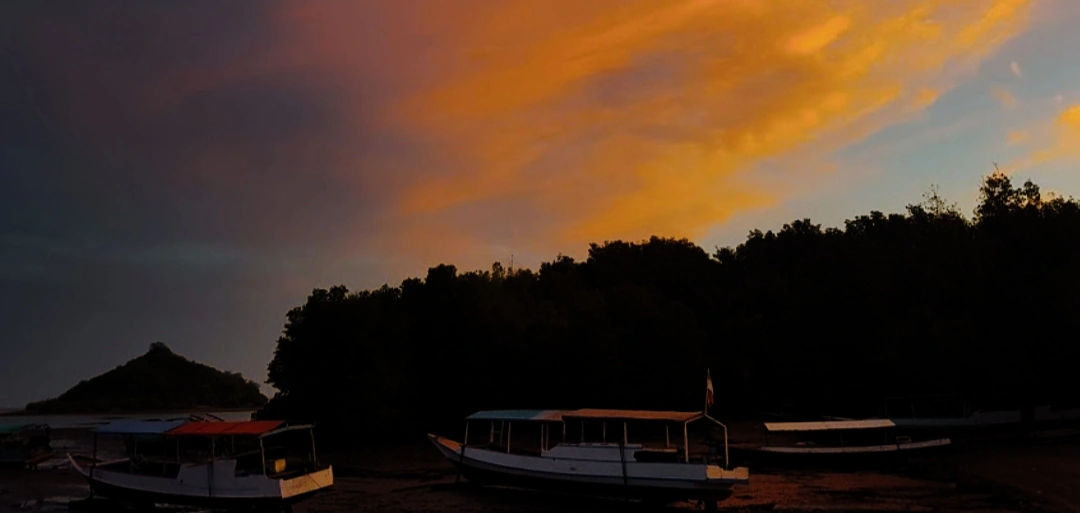 Wooden boats drawn up on the shore at Riung under an orange dusk sky